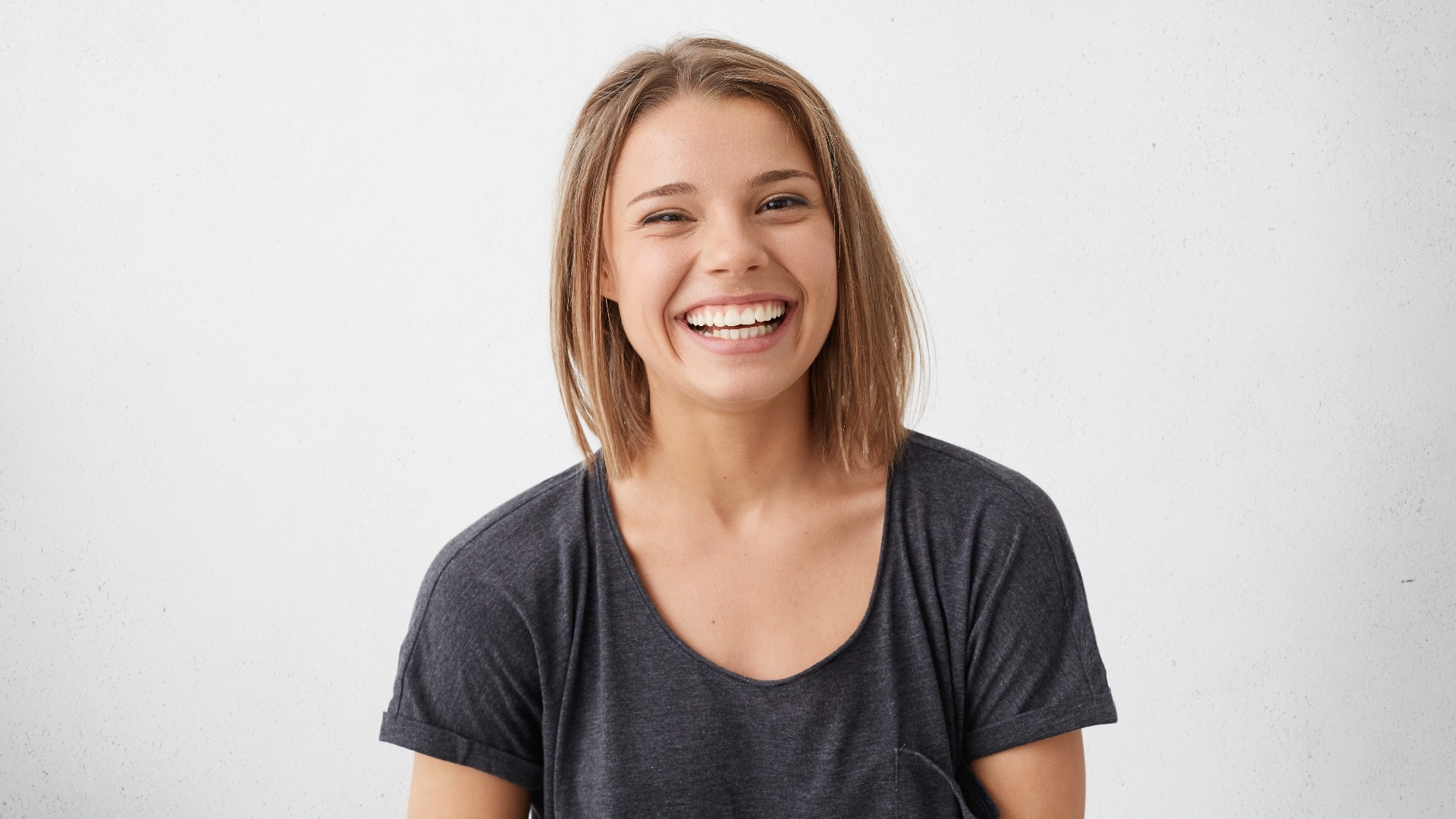 Attractive woman with short fair hair being very glad smiling with broad smile showing her perfect teeth having fun indoors. Joyful excited cheery femlae rejoicing after being proposed to marry